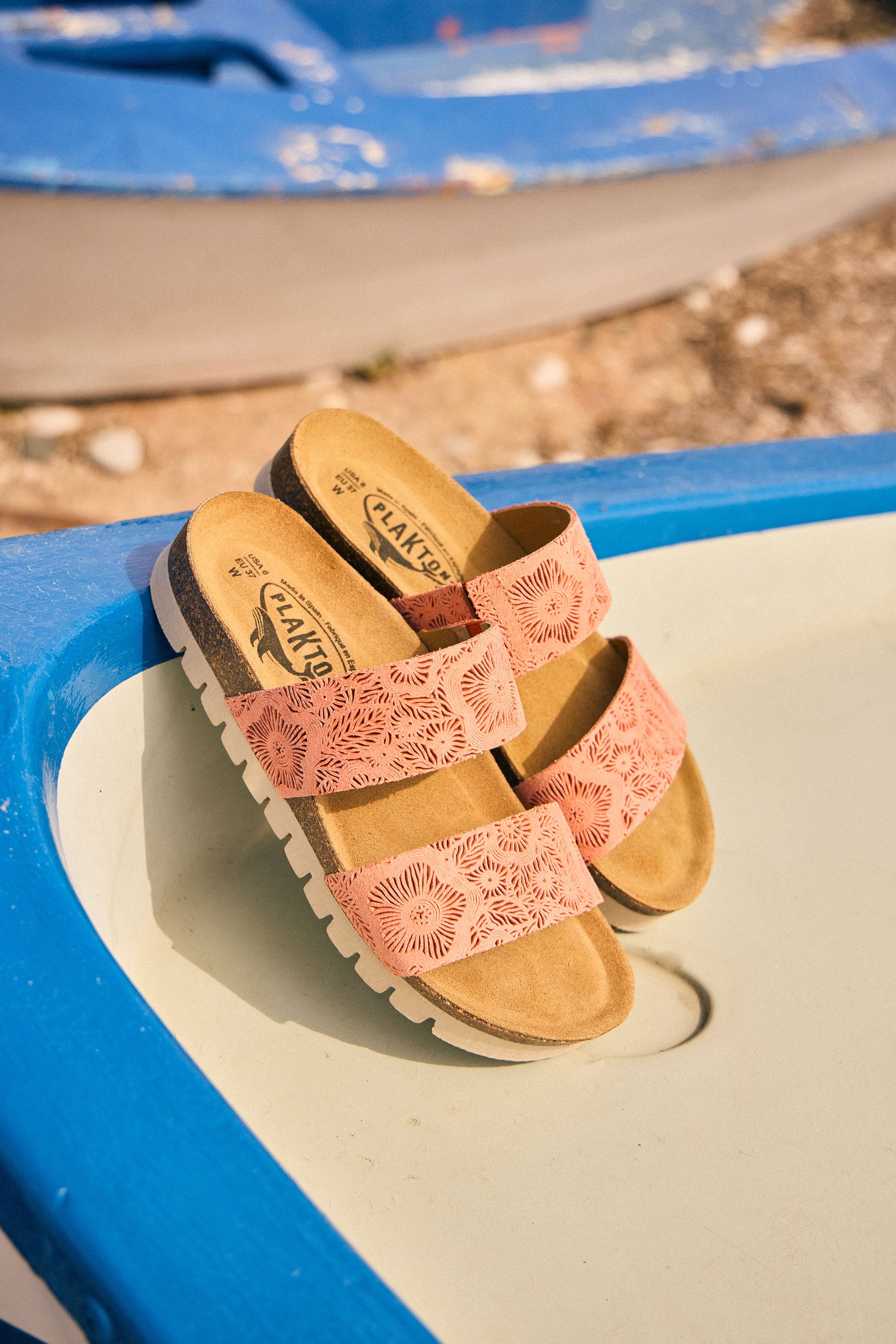 Plakton Brynn flat sandals in duranzo micro-suede with floral cutout straps and cork footbed resting on a blue boat, highlighting comfortable handmade summer sandals from Spain.