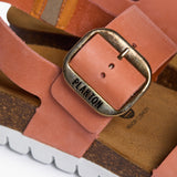 An extreme close-up focusing on the matte, velvety grain of the Peach nubuck leather. A sturdy metallic buckle embossed with "PLAKTON" anchors the strap, while the background highlights the porous, breathable texture of the natural Spanish cork, reinforcing a legacy of eco-conscious craftsmanship and organic beauty.
