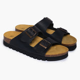 A pair of Beta sandals in Soft Black, angled to reveal the deep heel cups and the smooth transition of the handcrafted cork base. Dual adjustable straps with dark metallic buckles sit atop the plush suede-lined footbed, highlighting a design that balances timeless style with anatomical wisdom.