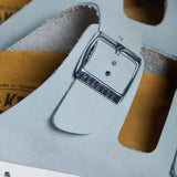 An extreme close-up of the Beta strap, focusing on the fine, velvety grain of the Soft Blue nubuck leather. A sturdy metallic buckle embossed with "PLAKTON" is the centerpiece, while the soft-focus background highlights the porous, sustainable Spanish cork, signifying premium handcrafted quality.