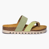 A side profile of the Bloom flat sandal, showcasing its low-profile, sustainable Spanish cork midsole. The multi-green suede straps overlap in varying earthy tones, providing a soft, textured look against the organic cork grain, all resting on a durable, flat black outsole for a grounded stride.