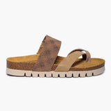 A side profile of the Bloom flat sandal, highlighting the slim, sustainable Spanish cork midsole. Overlapping suede straps in various desert-tan shades create a soft, architectural look against the organic cork grain, supported by a durable flat black outsole for a natural, grounded stride.