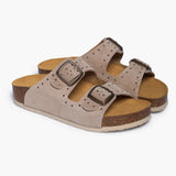 A pair of CP Beta sandals angled to reveal the deep anatomical heel cups carved from renewable cork oak. The dual adjustable taupe straps, decorated with polished studs and buckles, rest atop a soft suede-lined footbed, embodying Plakton’s "Nature’s Hug" philosophy where recycled elements meet raw, earth-born materials.