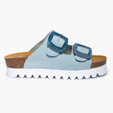 A side profile of the Calla sandal in Light Blue Nubuck, showcasing its flat, grounded foundation of sustainable Spanish cork. The pale blue leather straps provide a soft, velvety texture that contrasts beautifully with the organic, porous grain of the cork midsole, all supported by a durable high-grip outsole.