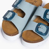 Looking directly down into the Calla footbeds, where the biologically contoured cork follows the foot's natural impression. The soft blue nubuck straps frame the "Plakton Memory Cushion" branding at the heel, illustrating a design that honors human anatomy through the use of renewable, earth-born materials.