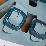 An extreme close-up focusing on the fine, matte grain of the Light Blue nubuck leather. A sturdy metallic buckle embossed with "PLAKTON" anchors the strap, while the soft-focus background reveals the breathable, sustainable texture of the natural Spanish cork, reinforcing a legacy of eco-conscious craftsmanship.
