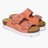 A pair of Calla sandals angled to highlight the deep, anatomical heel cups carved from renewable cork oak. The dual adjustable Peach straps feature brushed metallic buckles and rest atop a plush tan suede lining, embodying the "Nature’s Hug" philosophy—where artisan craftsmanship meets the pure, sun-warmed colors of nature.