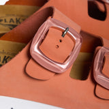 An extreme close-up focusing on the fine, matte grain of the Peach nubuck leather. A sturdy metallic buckle embossed with "PLAKTON" anchors the strap, while the soft-focus background reveals the breathable, sustainable texture of the natural Spanish cork, reinforcing a legacy of eco-conscious Mediterranean craftsmanship.