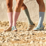 Two pairs of feet wearing colorful socks and sandals on a rocky ground.